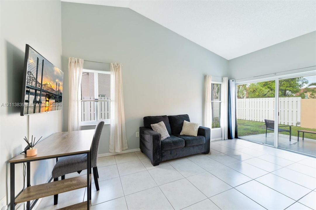Living area featuring vaulted ceilings, large-format tile flooring, and sliding glass doors providing access to a concrete patio