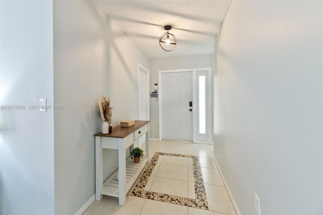 Entryway featuring tile flooring with decorative stone-tiled inlay, six-panel exterior door with sidelight, and matte black spherical pendant lighting