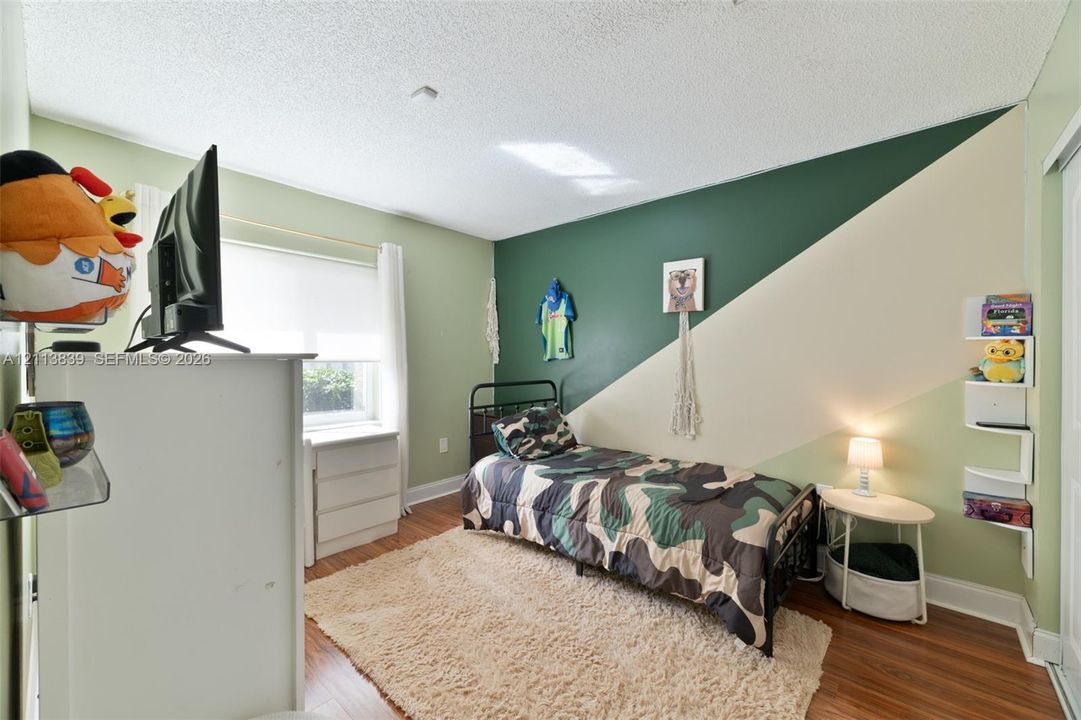 Bedroom featuring wood-finish flooring, a window with roller shade, and built-in wall-mounted shelving
