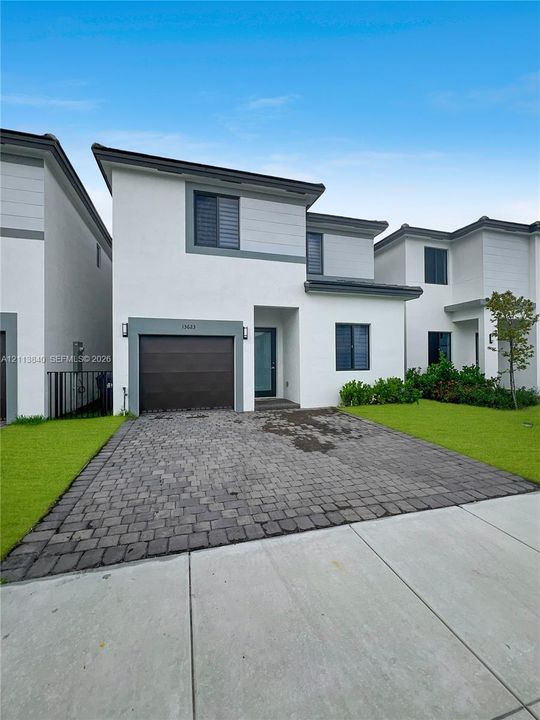 Contemporary exterior featuring smooth stucco finish, horizontal lap siding accents, integrated garage, paver driveway, and manicured lawn