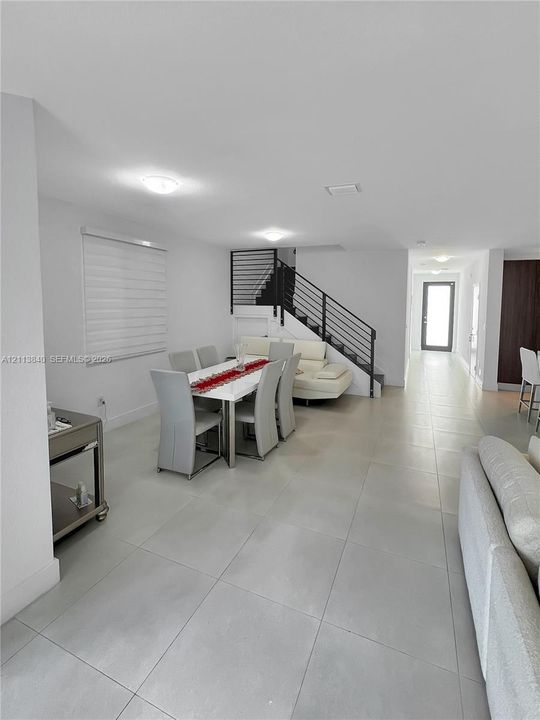 Large-format neutral tile flooring throughout the interior, staircase featuring a black metal horizontal railing, and recessed ceiling lighting