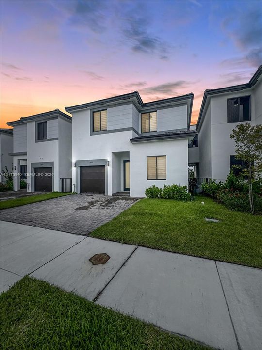 Modern two-story exterior featuring smooth stucco siding, contrast trim, integrated garage, paved driveway, and manicured landscaping