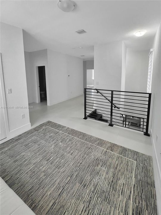 Minimalist interior space featuring matte-finish tile flooring, a black metal horizontal-bar railing, and flush-mount ceiling lighting