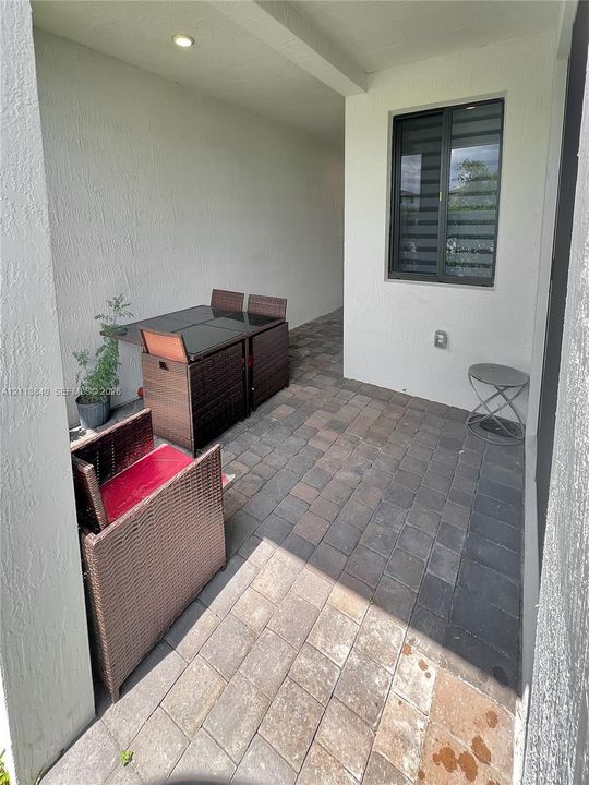 Covered patio featuring concrete paver flooring, textured exterior wall finish, and a framed window with adjustable horizontal blinds