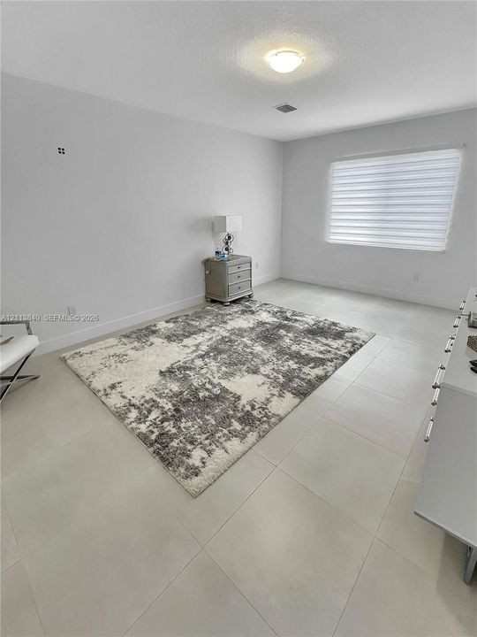 Neutral-toned tile flooring, minimalist white walls, and a window featuring adjustable horizontal blinds, centered by a flush-mount overhead light fixture