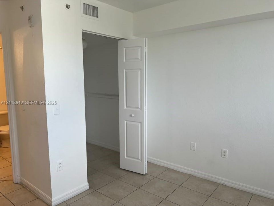 Interior space featuring neutral wall tones, large-format ceramic tile flooring, and a walk-in closet with a bi-fold door