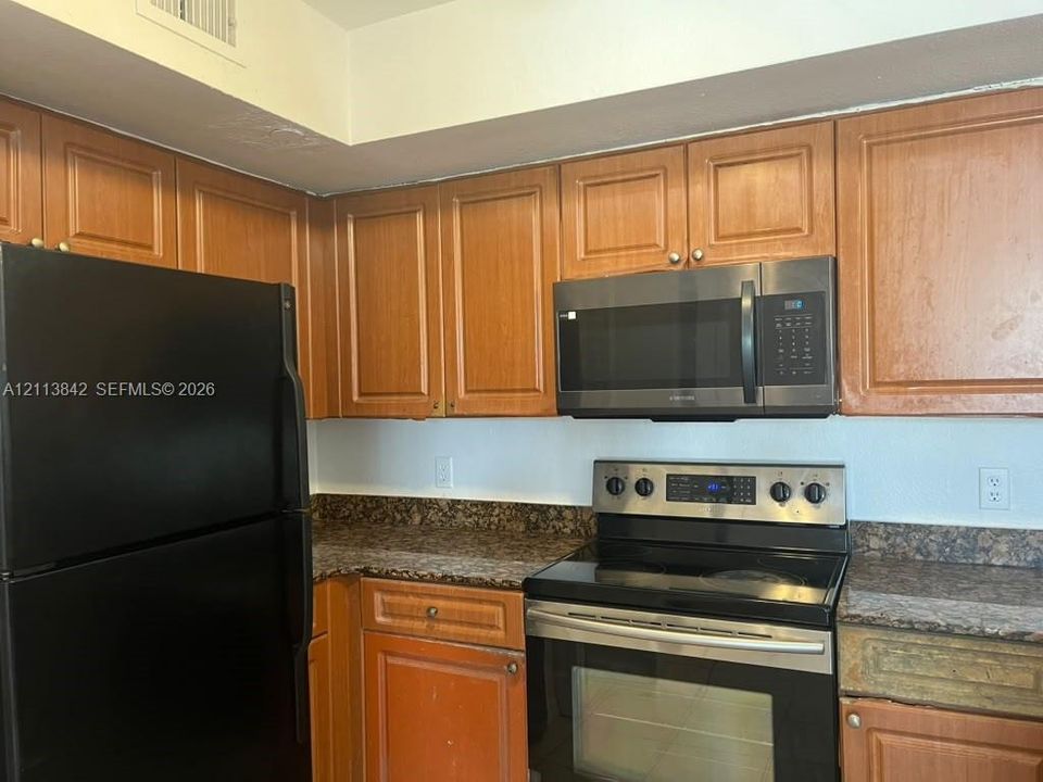 Kitchen featuring shaker-style wood cabinetry, stone-patterned laminate countertops, and a black appliance suite including a built-in microwave and electric range