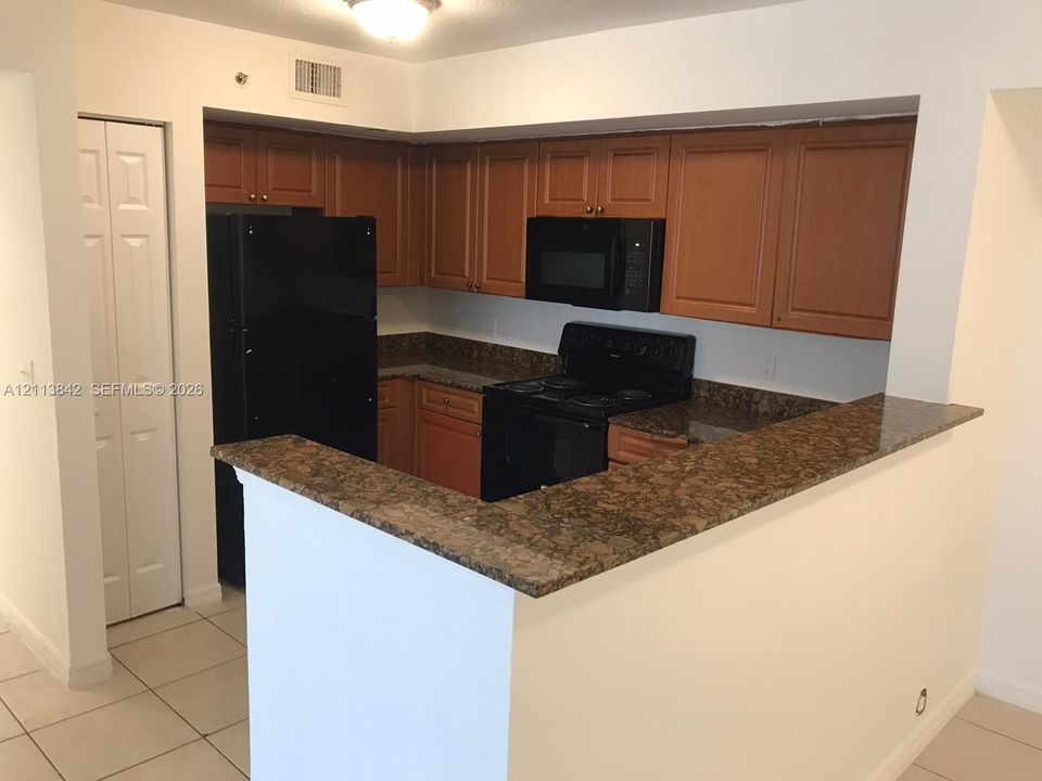 Kitchen featuring raised-panel wood cabinetry, stone-finish countertops, black appliance suite, and ceramic tile flooring