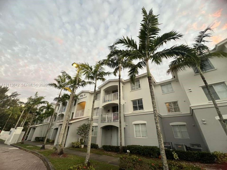 Multi-story exterior featuring a two-tone facade, private balconies with metal railings, and established palm tree landscaping