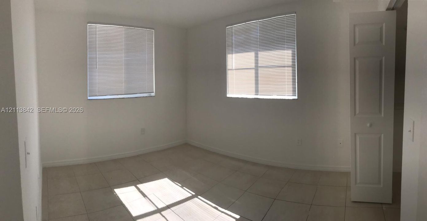 Neutral-toned tile flooring, dual windows with horizontal blinds, and a multi-panel interior door