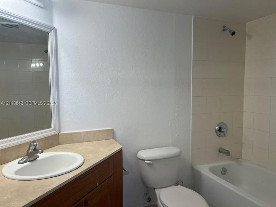 Bathroom featuring a wood-finish vanity with a stone-surfaced countertop, integrated oval basin, framed wall mirror, and a tiled shower-tub combination with chrome fixtures