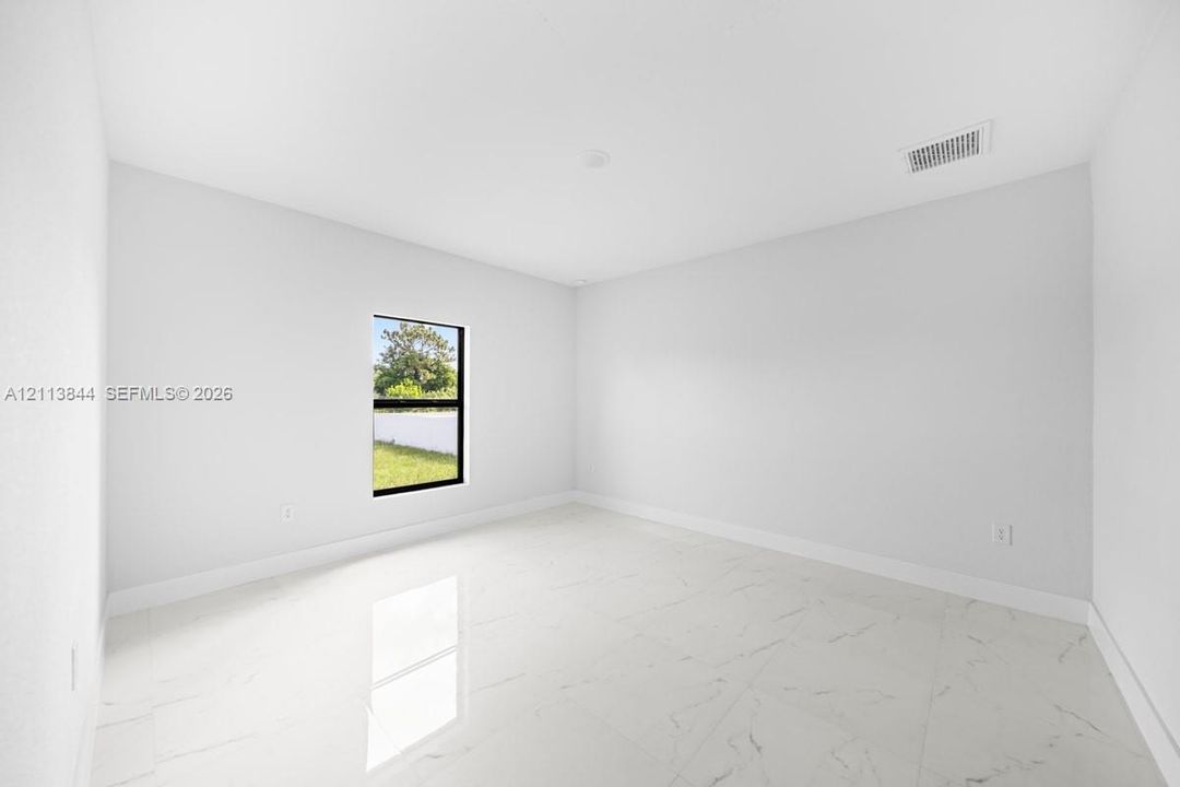Neutral interior space featuring polished tile flooring with a veined pattern, stark white walls, and a single-pane window with a black frame