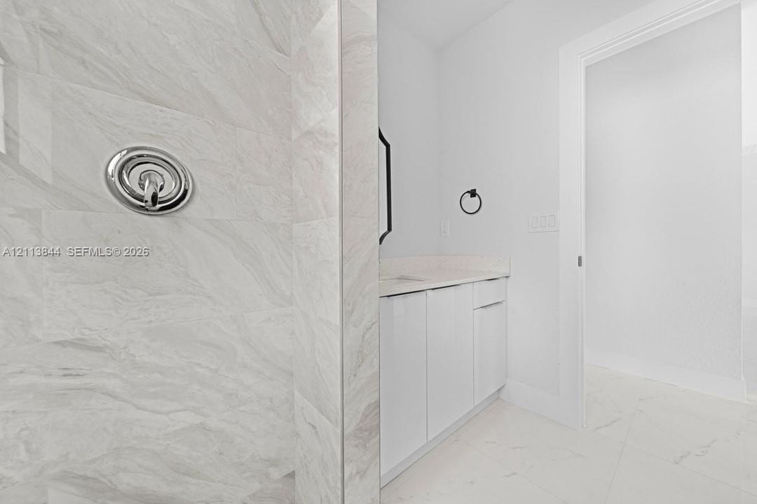 Shower featuring large-format stone-patterned wall tile and polished chrome plumbing fixtures, paired with a flat-panel vanity, light-toned countertop, and tile flooring