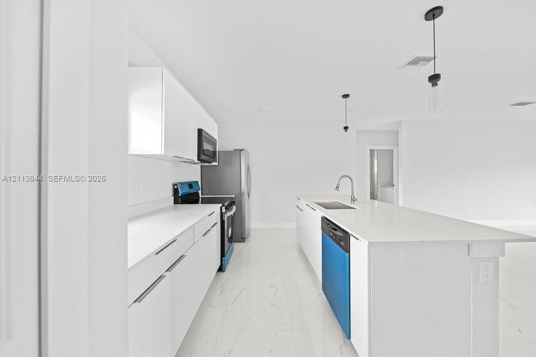 Kitchen featuring white flat-panel cabinetry, stone-finish countertops, central island with integrated stainless steel sink, large-format tile flooring, and pendant lighting