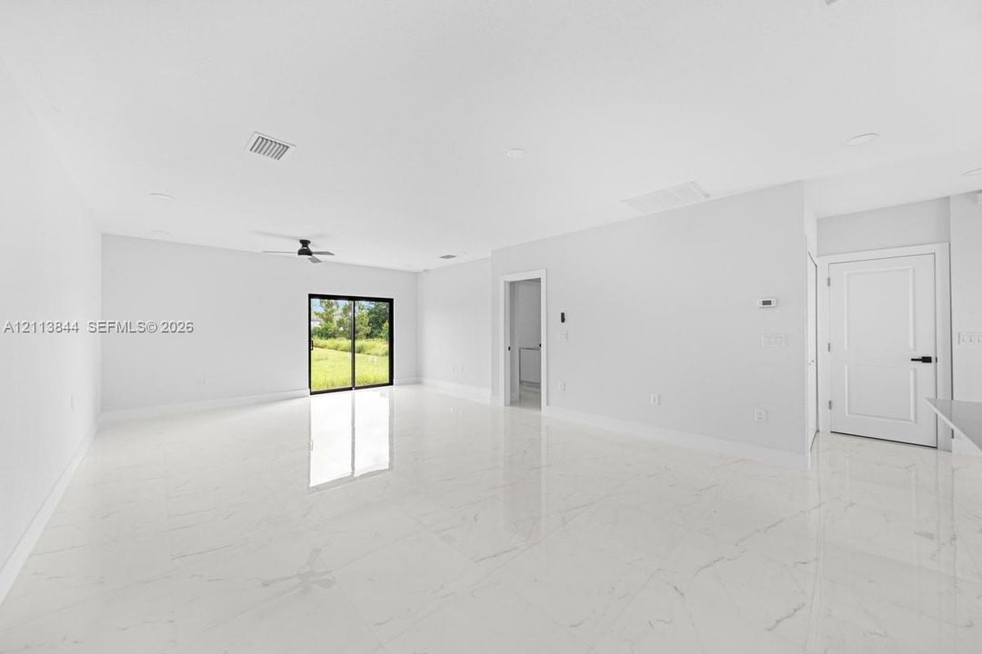 Open interior space featuring polished stone-finish tile flooring, recessed ceiling lighting, a matte black ceiling fan, and sliding glass doors