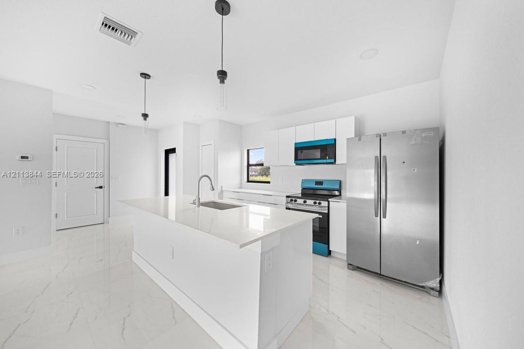 Kitchen featuring a central island with a quartz countertop, white flat-panel cabinetry, stainless steel appliances, and large-format tile flooring