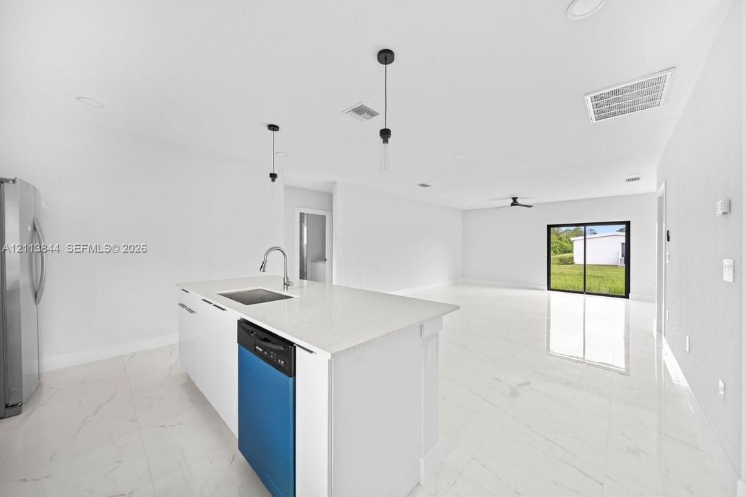 Kitchen featuring a center island with a quartz countertop, undermount sink, gooseneck faucet, and built-in dishwasher, complemented by light-toned large-format tile flooring and minimalist pendant lighting