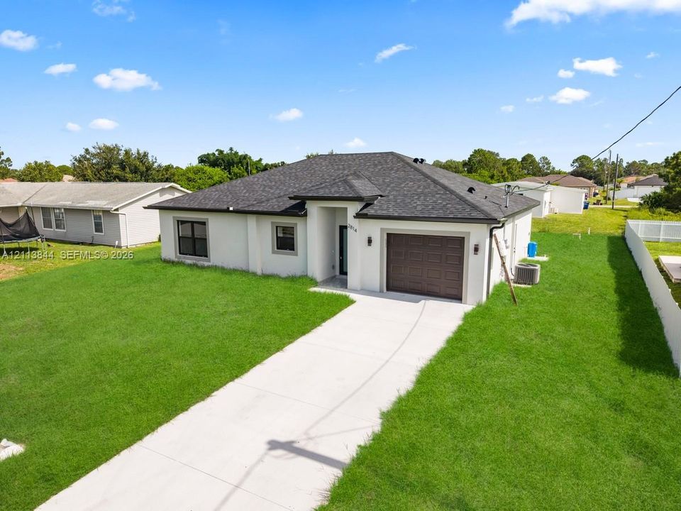 Single-story residence featuring a light-toned stucco exterior, dark asphalt shingle roof, attached garage with a segmented door, and a concrete driveway
