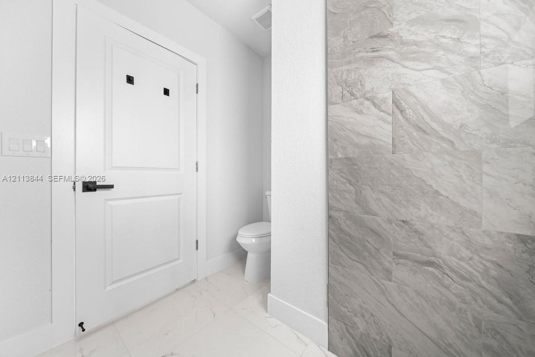 Restroom featuring a wall-mounted door with matte black hardware, large-format tile wall cladding, and polished stone-finish floor tiling