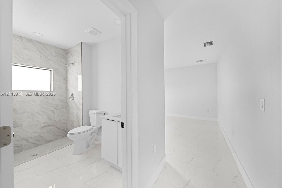 Bathroom featuring large-format light-toned tile flooring, walk-in shower with stone-style wall surround, transom window, and white cabinetry