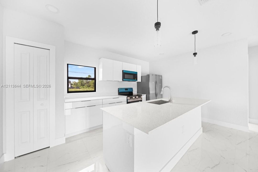 Kitchen featuring a center island with a stone-surface countertop, high-gloss white cabinetry, recessed ceiling lighting, pendant light fixtures, and white tile flooring