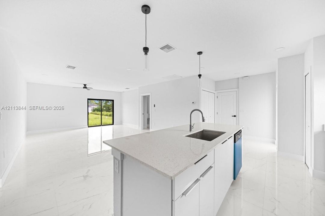 Kitchen island featuring a stone-composite countertop, undermount stainless steel sink, and sleek hardware, complemented by light-toned large-format tile flooring and minimalist pendant lighting