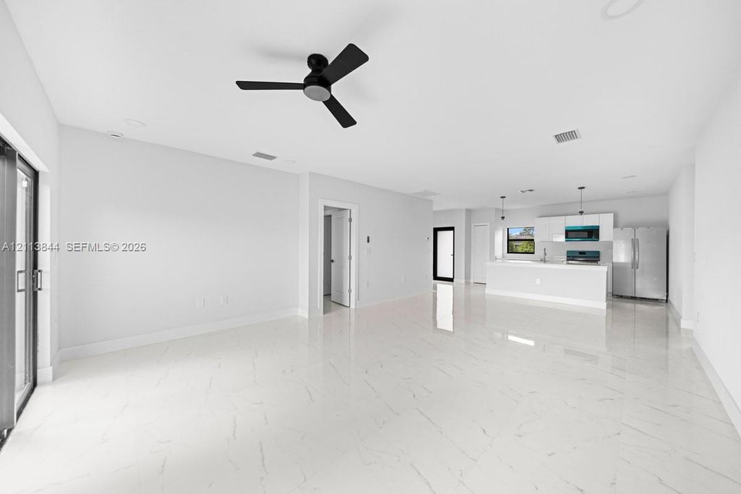 Open-concept interior featuring large-format stone-finish flooring, a matte black ceiling fan, recessed lighting, and kitchen cabinetry paired with stainless steel appliances