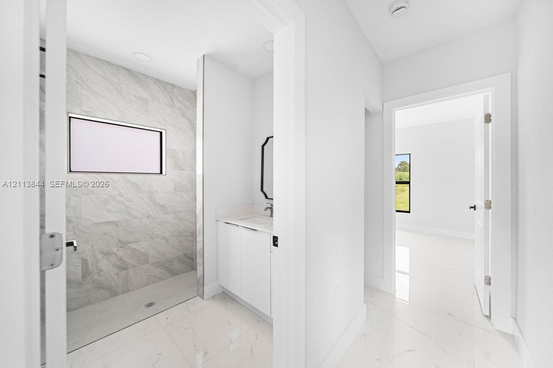 Walk-in shower featuring large-format tile walls, recessed lighting, and a pebble-tiled floor, complemented by a white vanity with a stone countertop and light-colored tile flooring