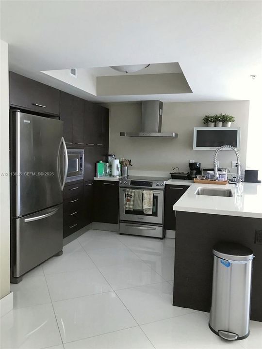 Kitchen featuring dark wood cabinetry, white stone-surface countertops, stainless steel appliances, a stainless steel chimney-style range hood, and polished tile flooring