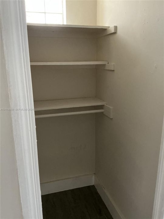 Storage closet featuring wood-finish flooring, two fixed shelves, and a built-in hanging rod