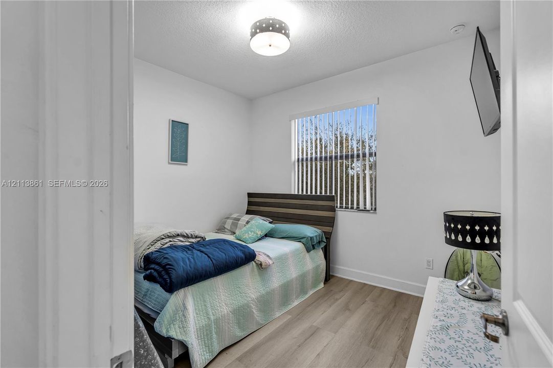 Room featuring wood-finish flooring, a neutral color palette, a single-window configuration with vertical blinds, and a semi-flush mount ceiling fixture