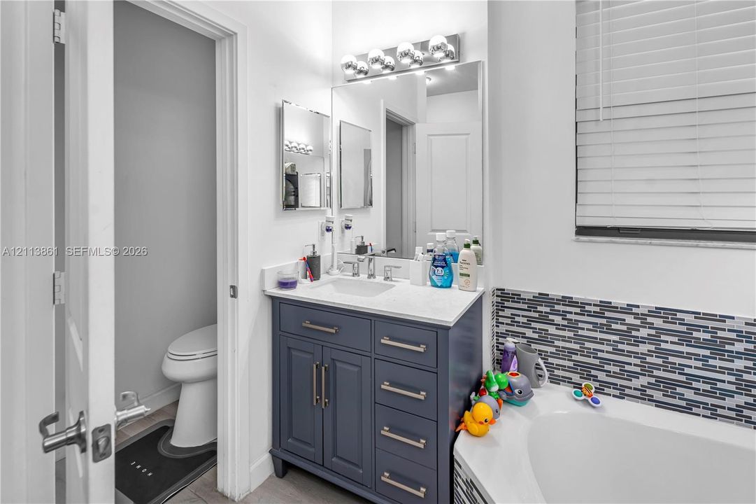 Vanity featuring a dark blue cabinet base, light-toned countertop, and undermount sink, accented by a full-width vanity mirror and multi-bulb light fixture