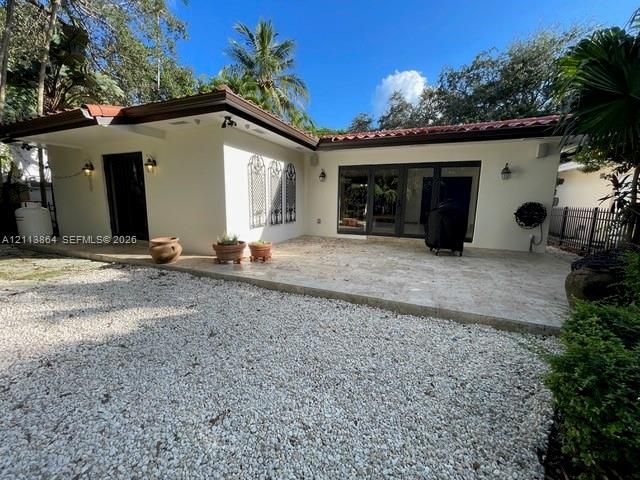 Exterior space featuring a neutral stucco finish, clay tile roof, expansive stone paver patio, multi-panel glass door systems, and decorative iron wall grilles