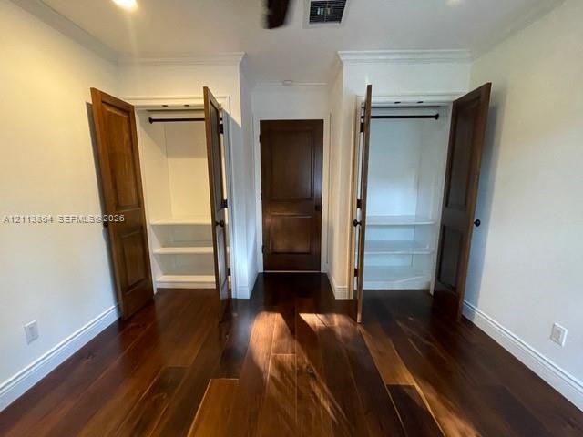 Room featuring dark-stained wood-finish flooring, two dual-door closets with built-in shelving, and a solid-core wood-finish swing door