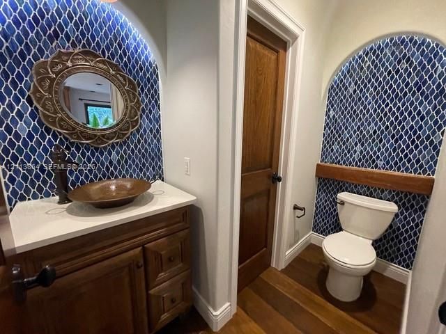 Custom vanity with stone countertop and copper vessel sink, arched alcoves with blue patterned tile work, wood-finish flooring, and solid wood interior door