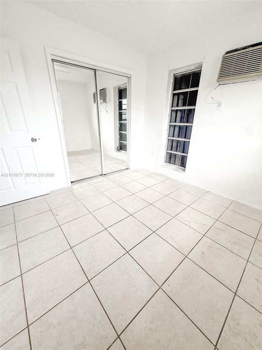 Room featuring ceramic tile flooring, mirrored sliding closet doors, and jalousie-style window