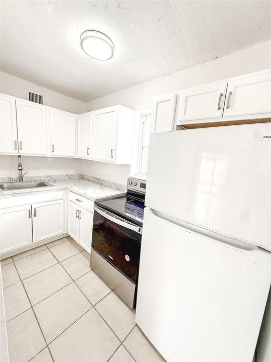 Kitchen featuring white shaker-style cabinetry, stone-pattern laminate countertops, stainless steel sink with a high-arc faucet, stainless steel range, and ceramic tile flooring