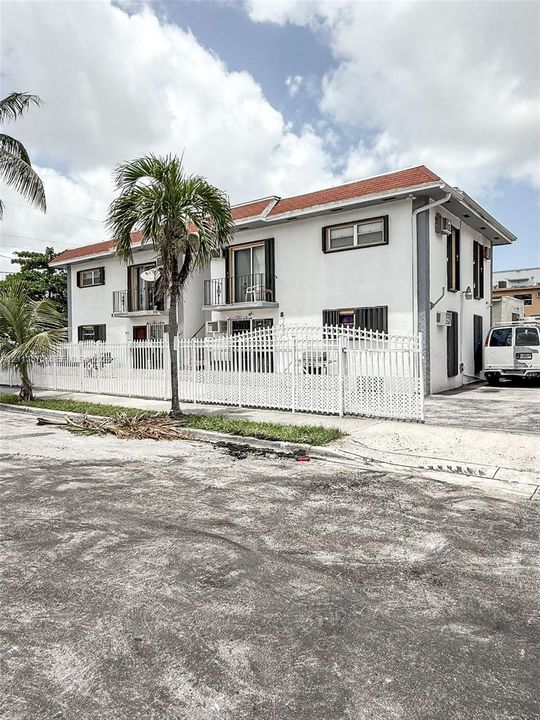 Two-story multi-unit exterior featuring a painted stucco finish, red tile roofing, second-story balconies, and a perimeter white metal fence