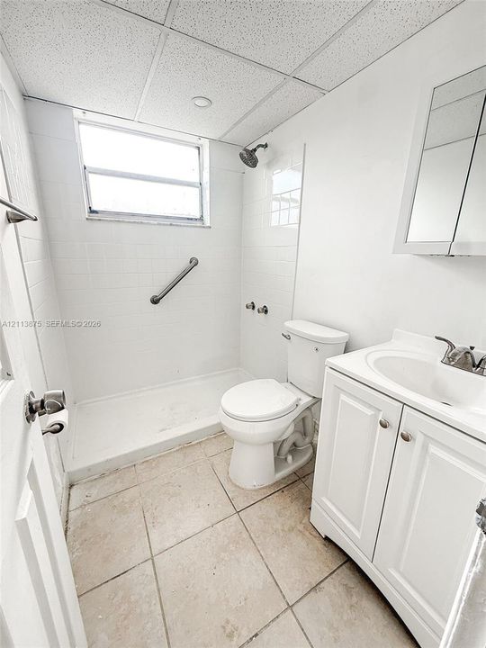 Bathroom featuring a white vanity cabinet with an integrated sink, tiled flooring, a walk-in shower stall with white wall tile, a metal grab bar, and a mirrored medicine cabinet