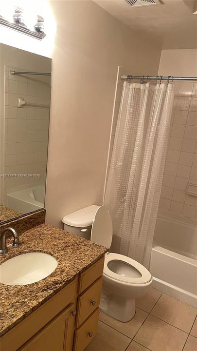 Bathroom featuring a vanity with a stone-finish countertop, undermount sink, multi-drawer cabinetry, large wall-mounted mirror, and a tub-shower combination with tiled surround