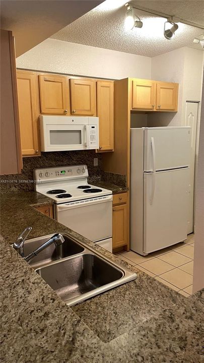 Kitchen featuring light wood cabinetry, stone-finish countertops, dual-basin stainless steel sink with pull-down faucet, white appliance package, and track lighting