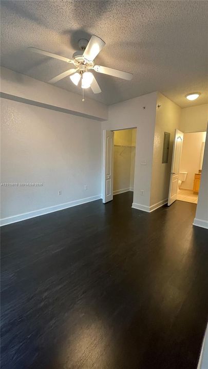 Dark-toned wood-finish flooring, ceiling fan with integrated lighting, recessed ceiling lighting, and walk-in closet