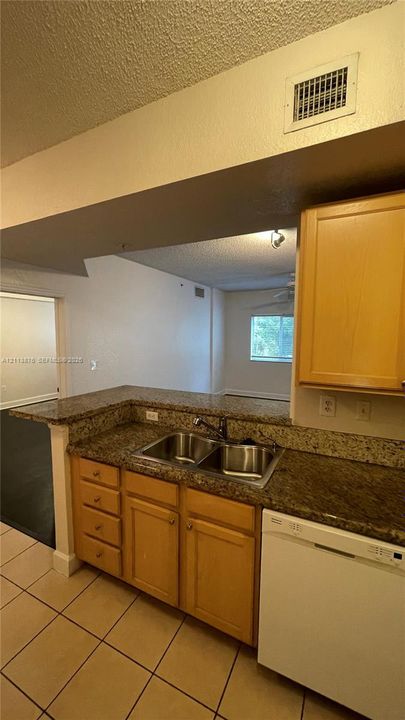 Kitchen featuring wood cabinetry, stone-surface countertops, a dual-basin stainless steel sink with a high-arch faucet, and tile flooring