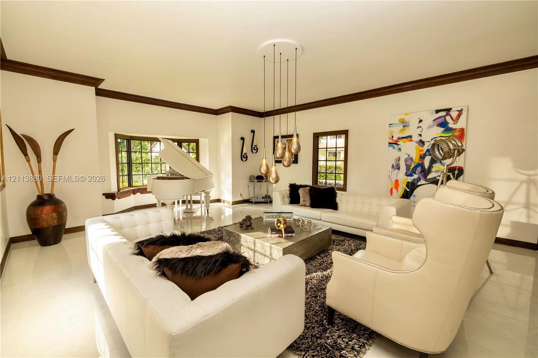 Living area featuring polished tile flooring, dark crown molding, a bay window, and a multi-pendant light fixture