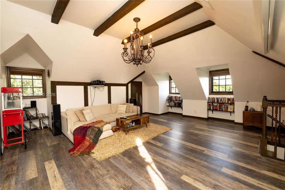 Vaulted ceiling featuring exposed wood beams, wood-finish flooring, multi-arm metal chandelier, built-in shelving, and dormer windows