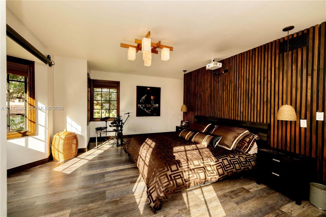 Interior space featuring a vertical wood-slat accent wall, wood-finish flooring, multi-pane windows with wood trim, a geometric multi-light chandelier, and integrated pendant lighting