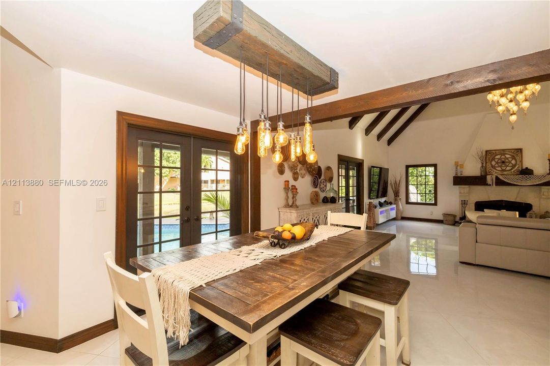 Custom timber beam lighting fixture with exposed filaments, dark-stained wood ceiling beams, multi-pane glass doors, and polished stone flooring