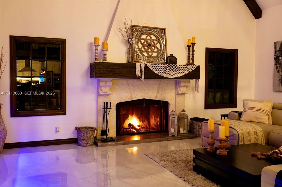 Floor-to-ceiling fireplace featuring a textured stone surround, heavy timber mantel, and vaulted ceilings, punctuated by dark-frame grid windows