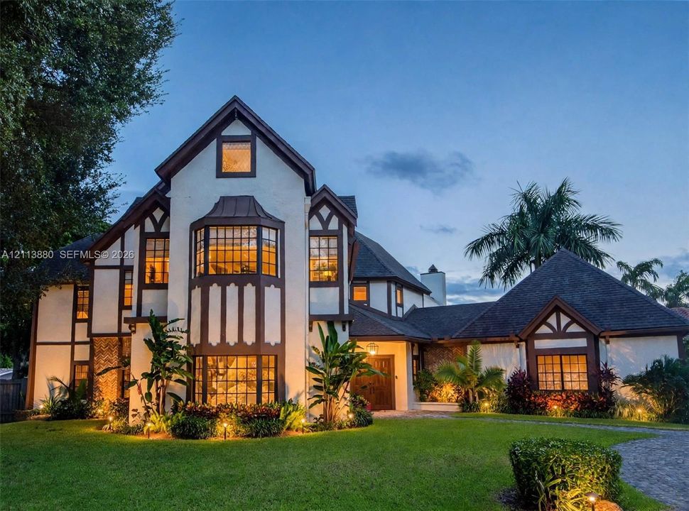 Tudor-style exterior featuring a multi-gabled roofline, decorative half-timbering, large bay windows, and a paved stone driveway