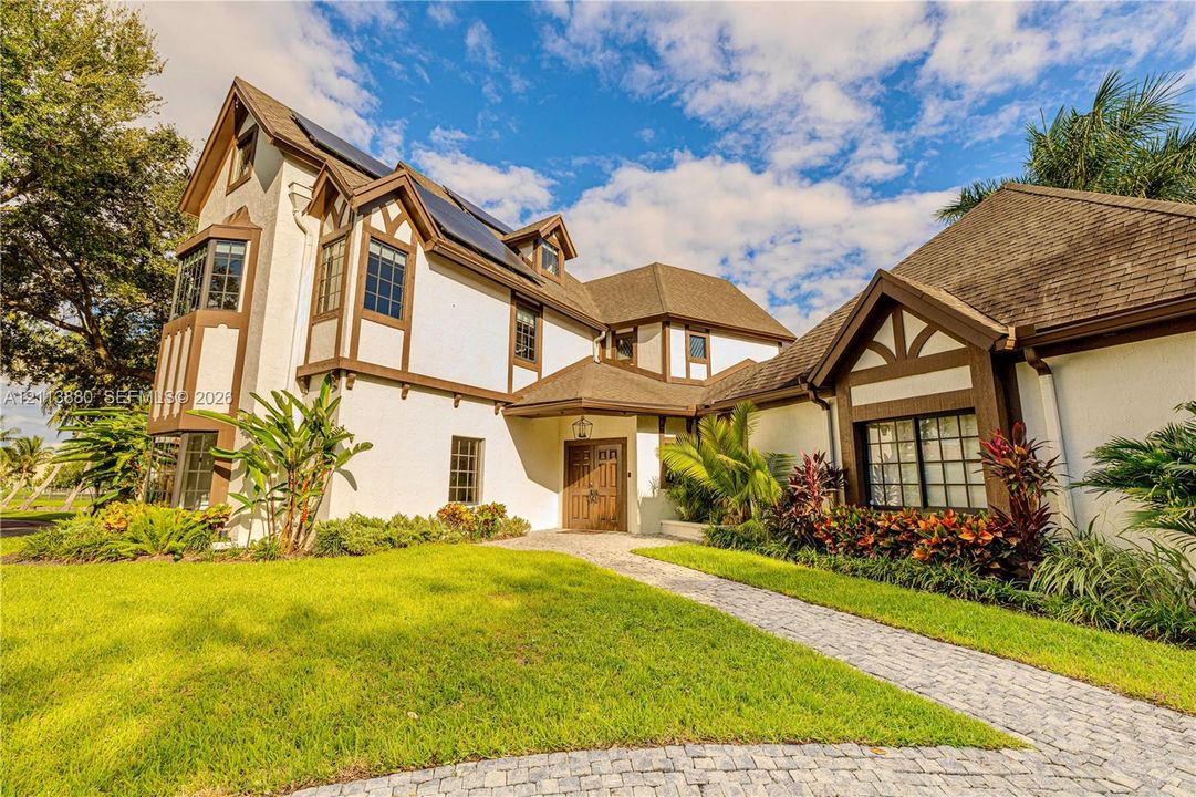 Tudor-style exterior featuring stucco facade with timber framing, multi-pane windows, solar panel array, and paver walkway